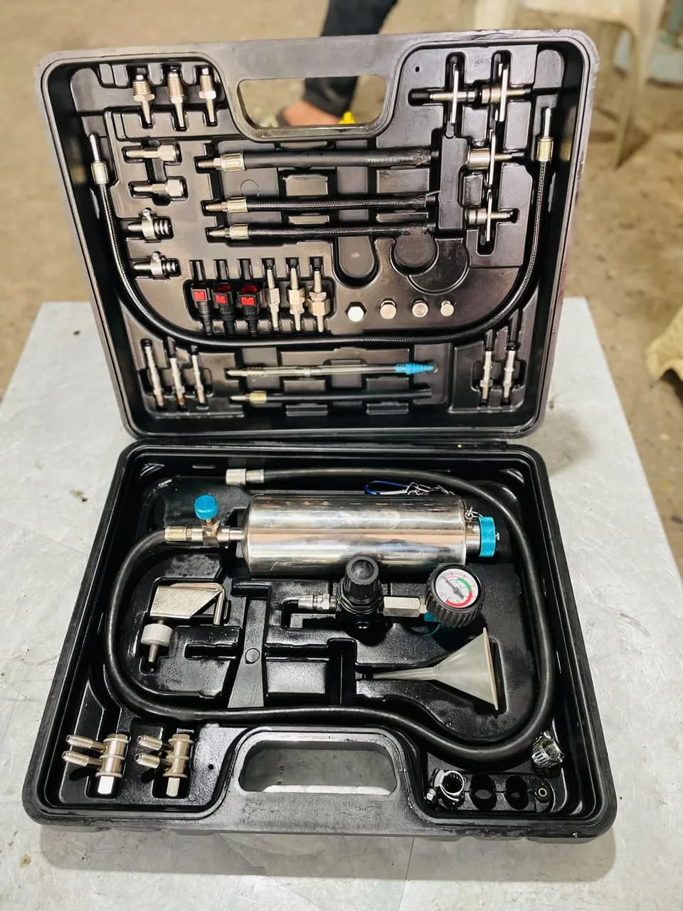 Open case of a pressurised fuel-system cleaning and tuning kit with canister, pressure gauge, hoses and engine adapters