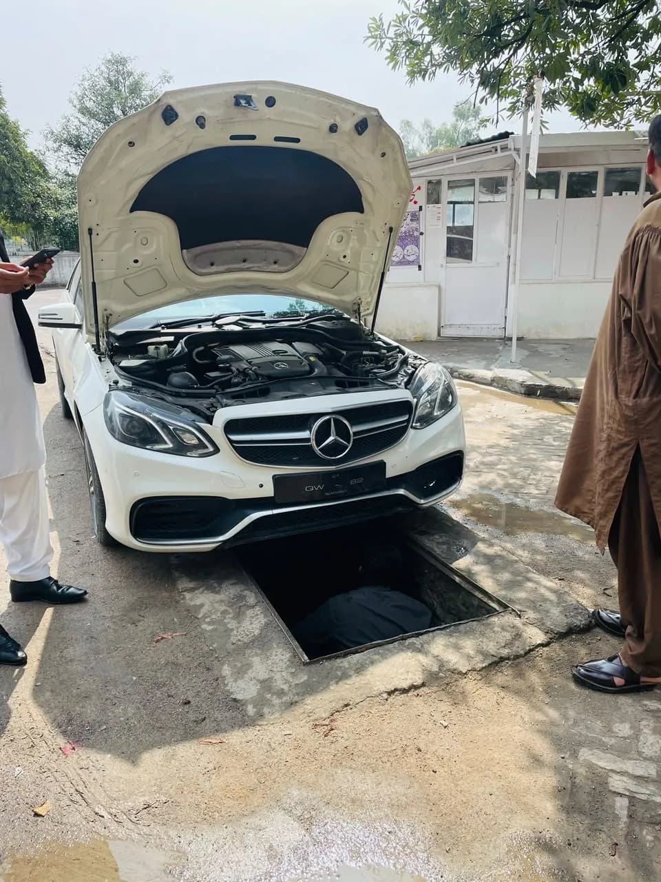 White Mercedes-Benz E-Class with its bonnet open, parked over the workshop's service pit