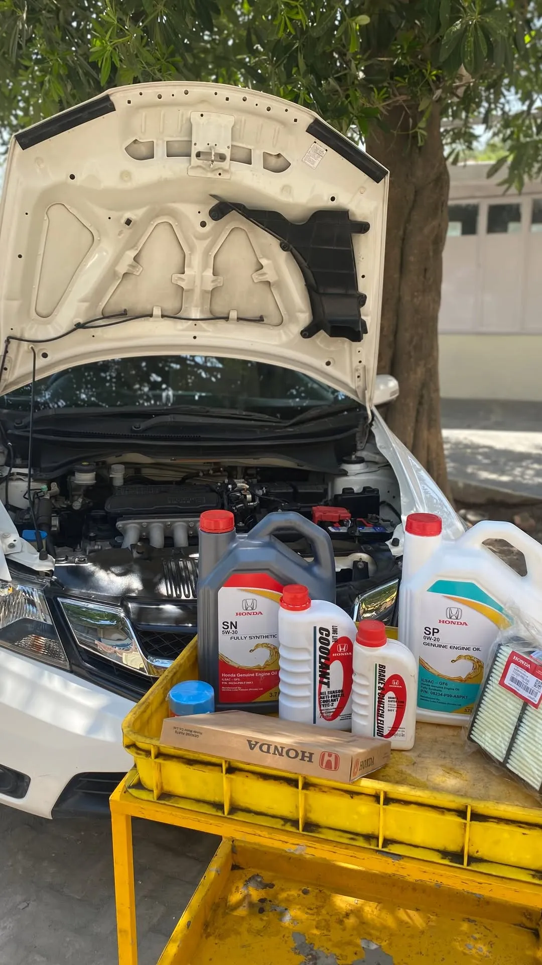 Engine oil, coolant and filters on a yellow trolley beside a car with its bonnet open