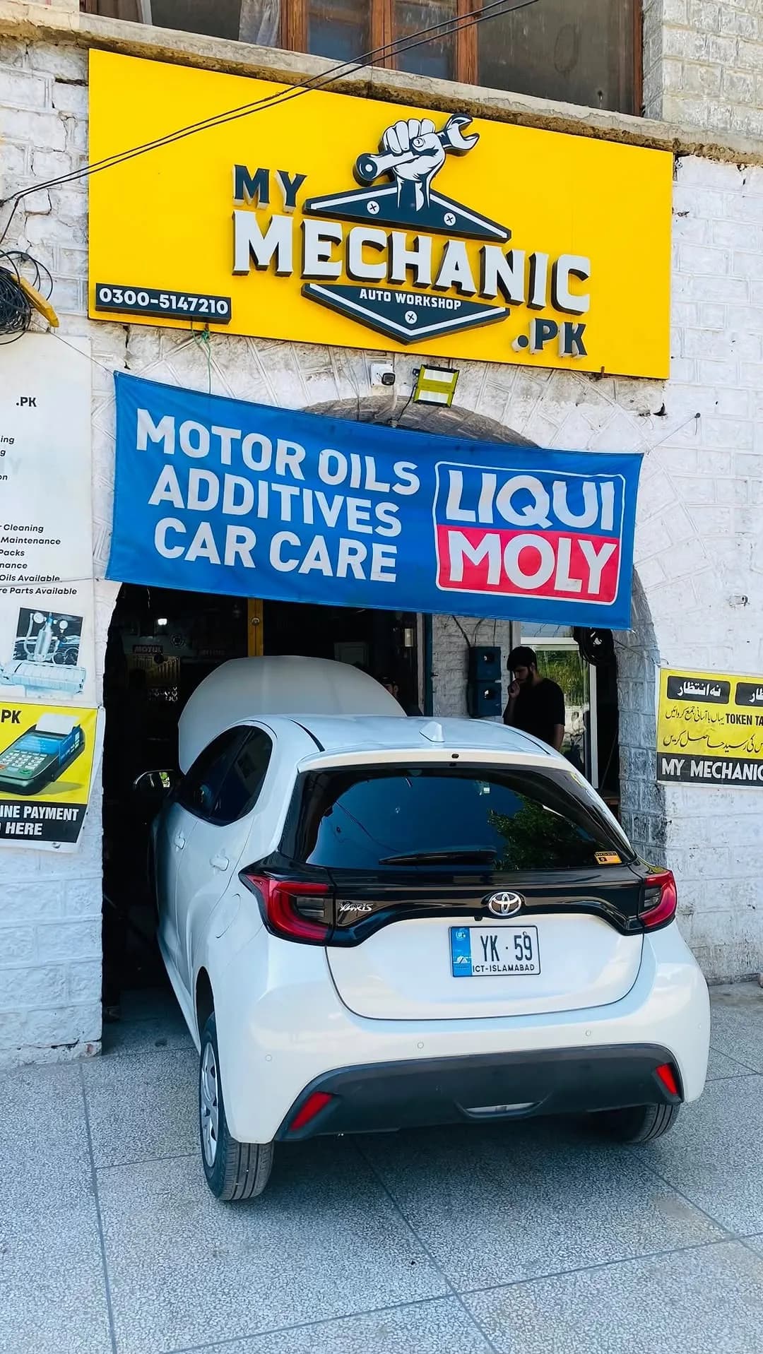 My Mechanic.pk workshop front with its yellow sign and a Liqui Moly motor-oil banner, a white Toyota Yaris parked in the service bay