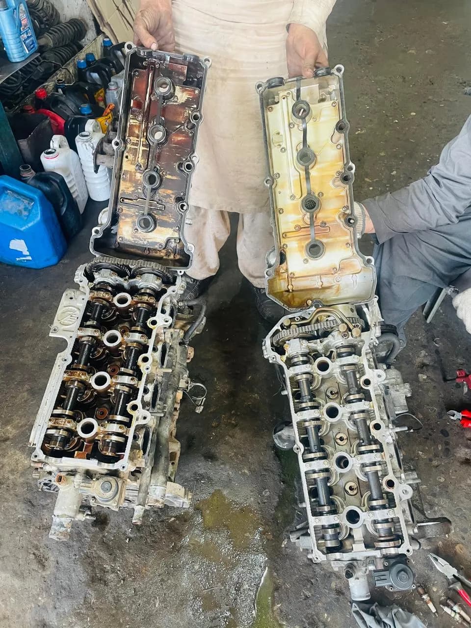 Two Japanese cylinder head assemblies side by side on the workshop floor during a head swap