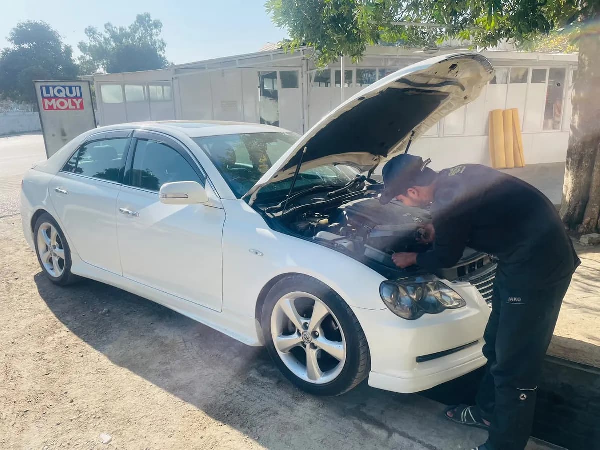 My Mechanic technician checking the engine of a white Toyota Mark X outside the workshop, beside a Liqui Moly sign