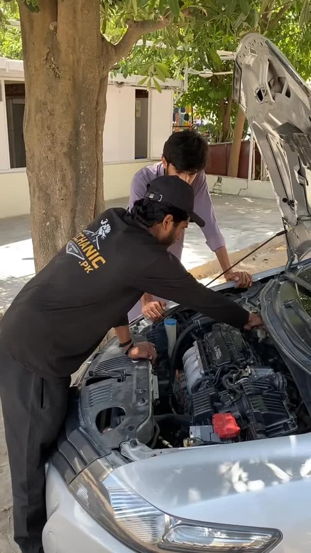 Two My Mechanic technicians working under the open bonnet of a car outside the workshop